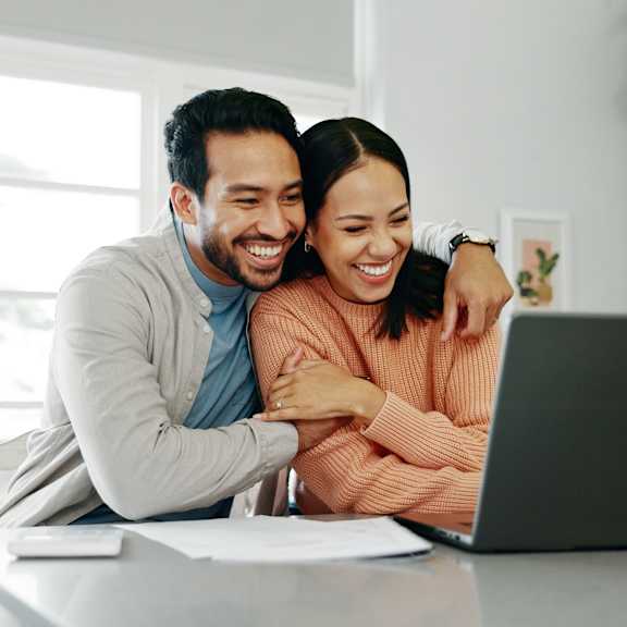 A man and woman are sitting at a table looking at a laptop screen.
