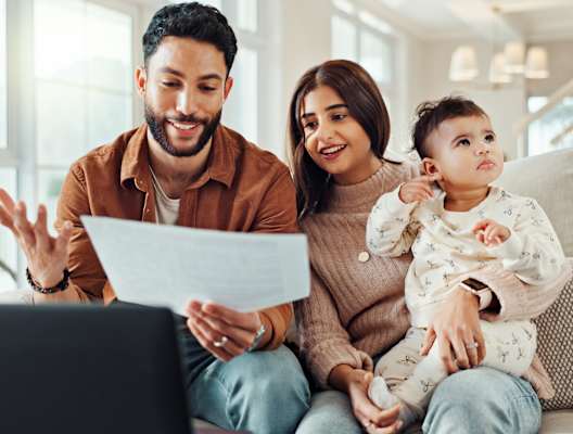 A family of three is sitting on a couch with a laptop in front of them.
