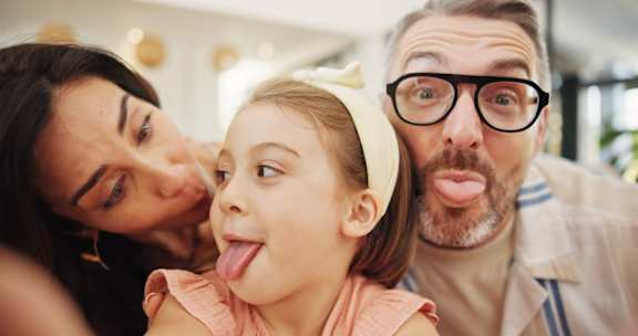 A man and a woman are making funny faces with a little girl.
