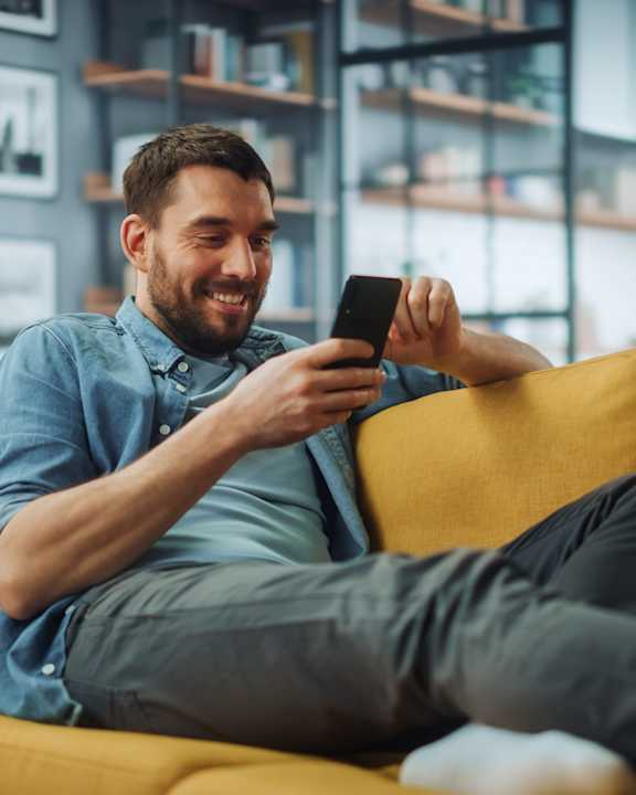 A man is sitting on a yellow couch and using a smartphone.