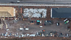 A construction site with a large building in the background and several vehicles and equipment scattered around the site.
