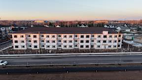 A large white building with a brown roof is surrounded by a parking lot.