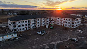 A sunset view of a large white building with a parking lot in front.