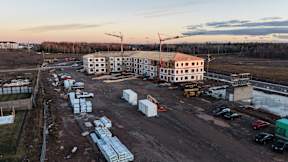 A construction site with a large building under construction and various vehicles and materials scattered around.