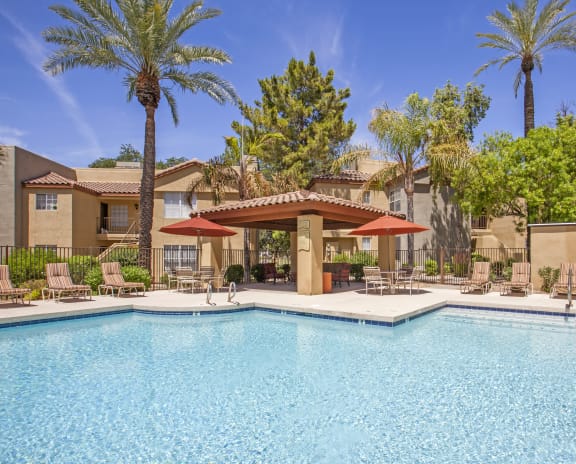 a swimming pool with chairs and umbrellas at a resort with trees