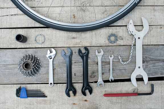 A collection of bicycle repair tools is laid out on a wooden surface.