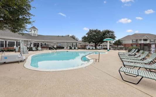 A pool area with sun loungers and a building in the background.