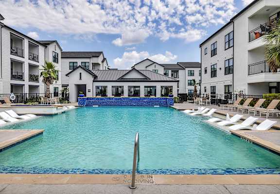 A pool surrounded by lounge chairs and buildings in the background.