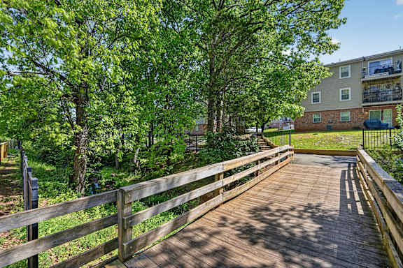 A wooden bridge in a park with trees and a building in the background.