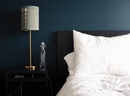 A bed with white pillows and a lamp on a side table at The Marquee Apartments, North Hollywood, California