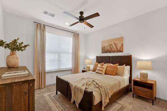 A bedroom with a bed, nightstand, and a plant on a wooden table.