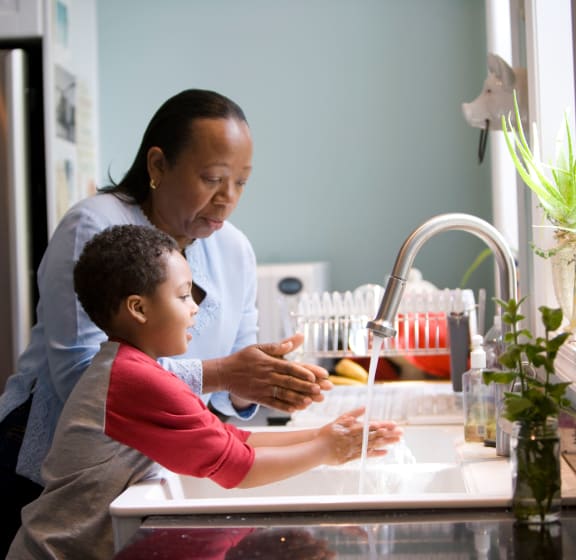 a woman and child wash their hands at a kitchen sink