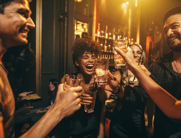 Group of people are toasting with drinks in a dimly lit bar at AMP 30 Apartments, San Diego, CA, 92116