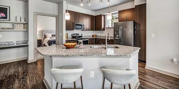 A kitchen with a granite countertop and white bar stools.
