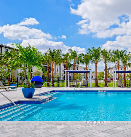 a large swimming pool with palm trees and buildings in the background