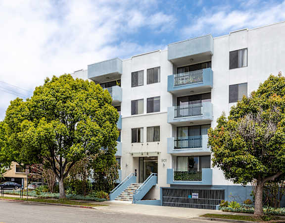 a white apartment building with a blue staircase and two trees in front of it