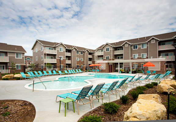 A swimming pool surrounded by chairs and umbrellas in front of apartment buildings.