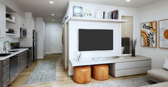 a living room with a large tv on the wall and a kitchen in the background