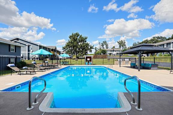 A large swimming pool surrounded by a fence and lounge chairs.