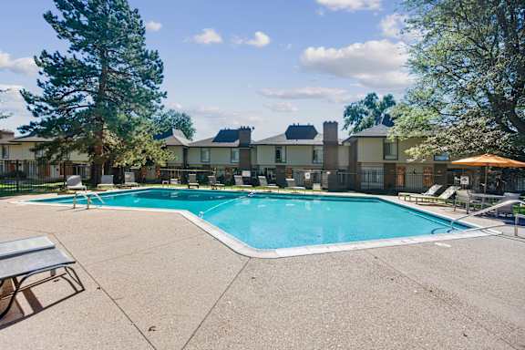 A swimming pool surrounded by a concrete patio and trees. at The Lex At Lowry, Denver, Colorado