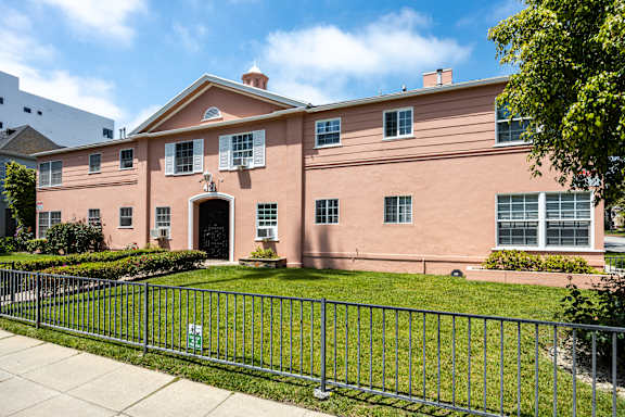 a pink building with a green lawn and a metal fence in front of it