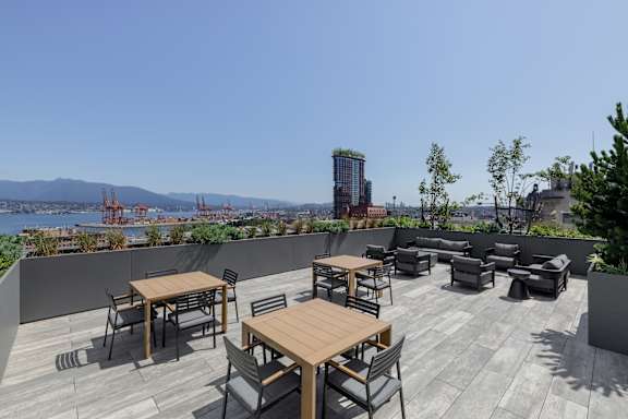 A rooftop patio with wooden tables and chairs overlooking a cityscape.