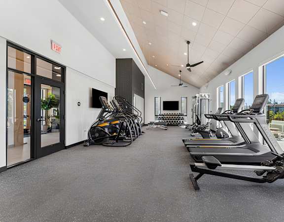A gym with treadmills, exercise bikes, and a ceiling fan.
