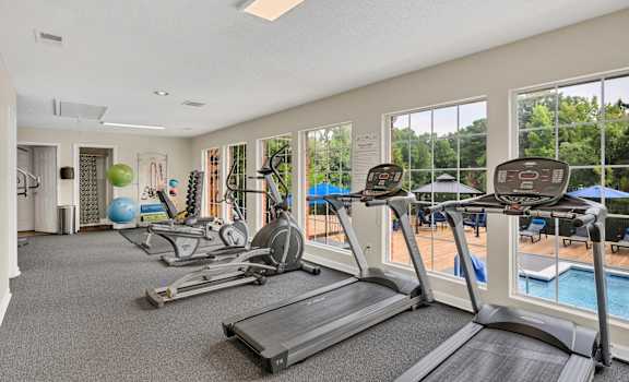 a gym with cardio machines and windows with a pool