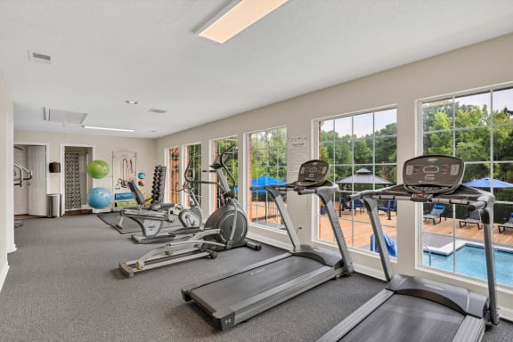 a gym with cardio machines and windows with a pool