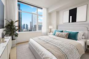 A bedroom with a large bed and a city view through the window.