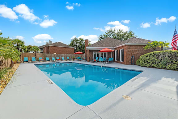 A swimming pool in a backyard with a house and palm trees in the background.