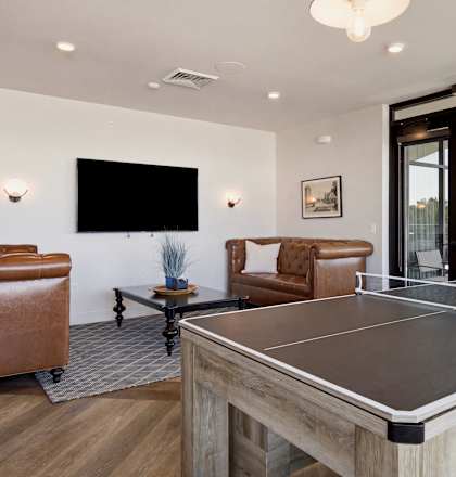 A ping pong table is in the middle of a living room with a couch and a chair.