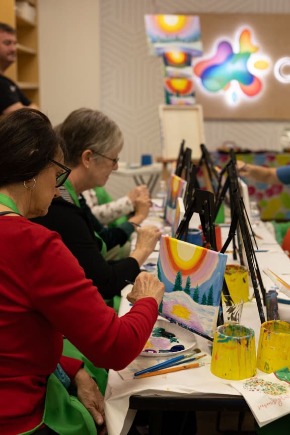 a group of women sitting at a table doing art on canvases