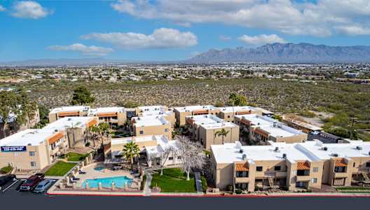 A large apartment complex with a pool in the foreground and a mountainous landscape in the background.