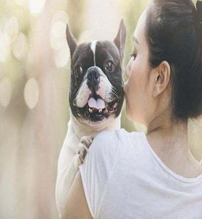 a woman kissing a small dog on her face