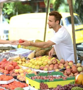 a man handing a fruit to a woman at a fruit stand