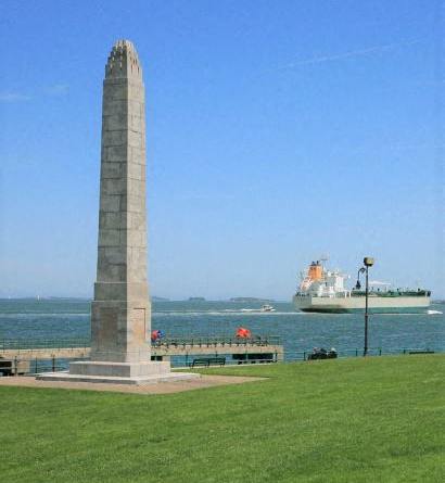 A monument stands in a grassy field with a large ship in the background.