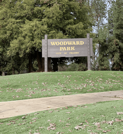 a sign for woodward park at the top of a grassy hill