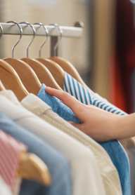 A person is holding a striped shirt in front of a rack of clothes.