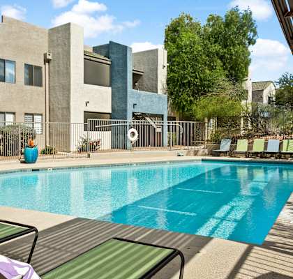 A pool surrounded by lounge chairs and a building in the background.