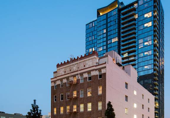 A tall building with a pinkish hue stands in front of a modern skyscraper.
