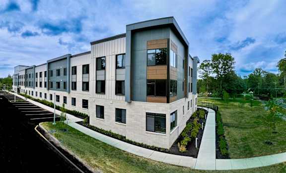 A modern building with a curved design and large windows is surrounded by a well-maintained lawn and a paved walkway.