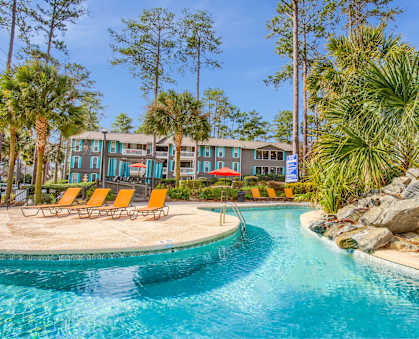 A swimming pool surrounded by palm trees and a building in the background.