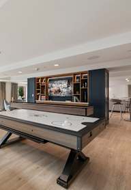 A billiard table is in the middle of a room with a white table and chairs.