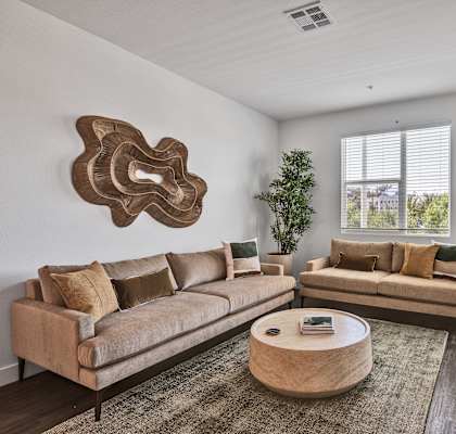 A living room with a beige sofa, a round coffee table, and a large decorative piece on the wall.