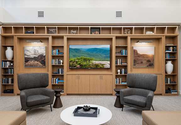 A living room with two chairs, a table, and a bookshelf with pictures on it.