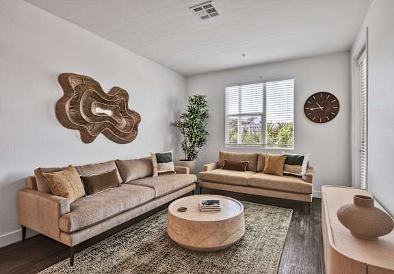 A living room with a beige sofa, a round coffee table, and a large decorative piece on the wall.