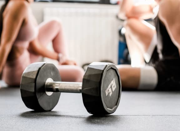 a dumbbell on the floor next to two women in the gym