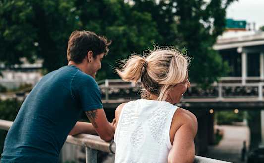 A man and a woman are standing close together on a bridge.