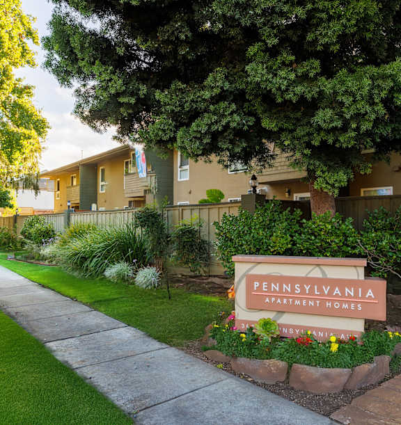 A sign for Pennsylvania Apartments is surrounded by flowers and greenery.